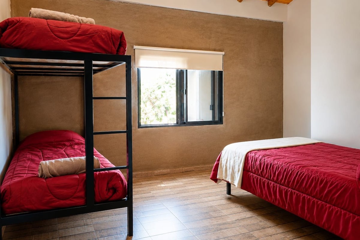 A room with a bunk bed, a single bed, and a window with a view.