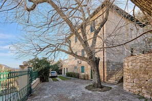 A stone building with a tree in front, a green gate, and a car parked nearby. - Green Horizon (Dubrovnik)