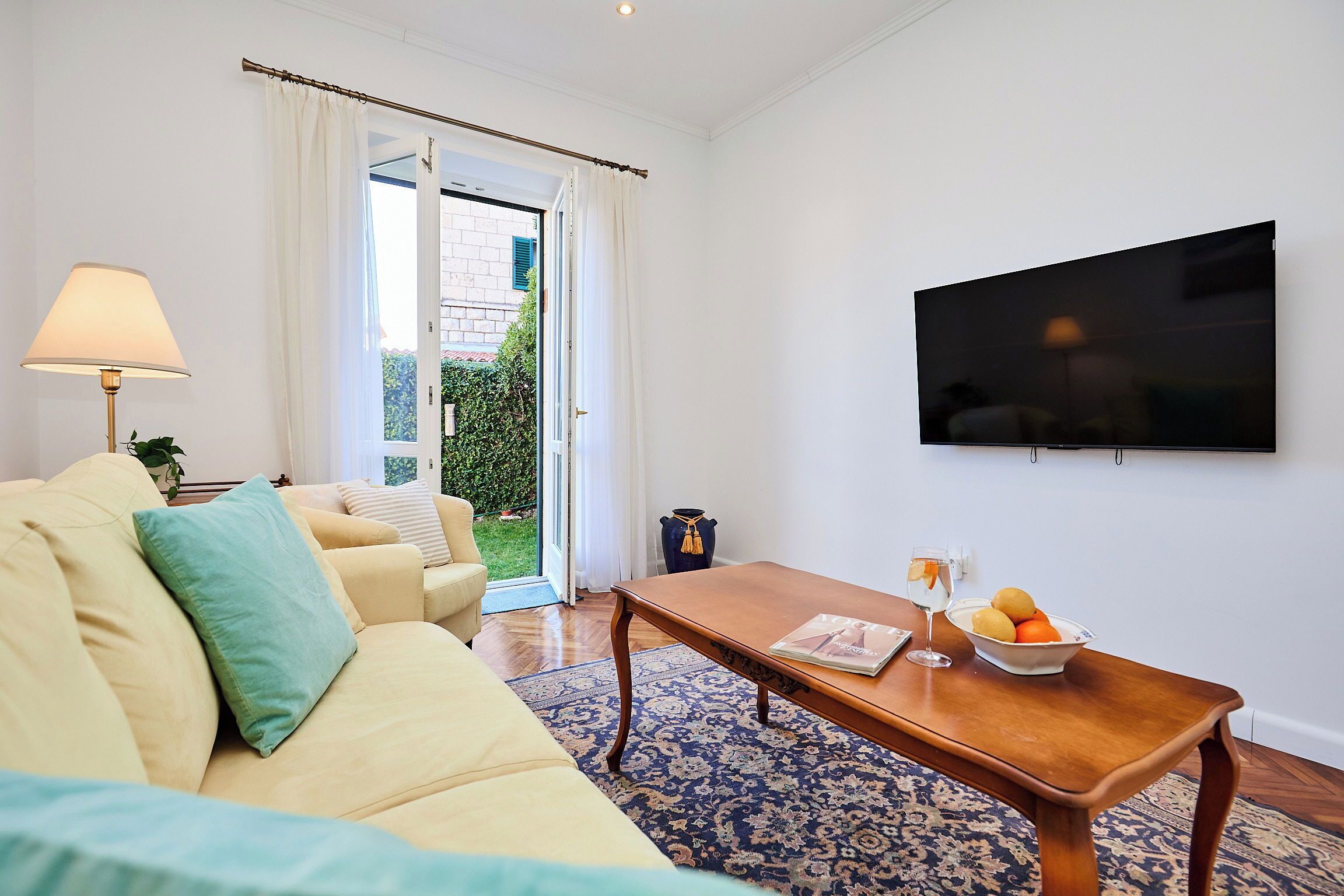 A living room with a sofa, a coffee table with fruit, a TV, and a view of the outdoors.