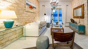 A living room with a stone wall, a white sofa, a glass coffee table, a wooden chair, and a blue lamp. - Villa Melyssaia, Private Pool and Garden, Spacious Furnished Terrace, Zakynthos (Zakynthos)