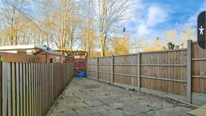 Ein gepflasterter Garten mit Holzzaun, einem Backsteinbau und im Hintergrund kahlen Bäumen.