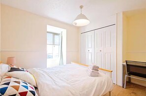 A bedroom with a bed, a desk, a chair, a window, and a door. - Apartment - Sleeps 5 - Private Garden (London)
