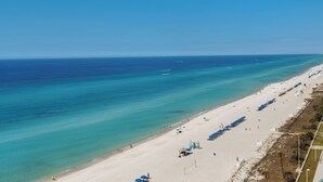 Ein Strand mit klarem türkisfarbenem Wasser, einem Sandufer und mehreren blauen Sonnenschirmen.