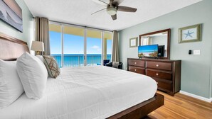 Ein Hotelzimmer mit einem großen Bett, einem Deckenventilator, einem Schminktisch, einem Fernseher und Blick aufs Meer.