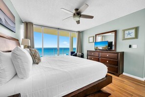 Ein Hotelzimmer mit einem großen Bett, einem Deckenventilator, einem Schminktisch, einem Fernseher und Blick aufs Meer.