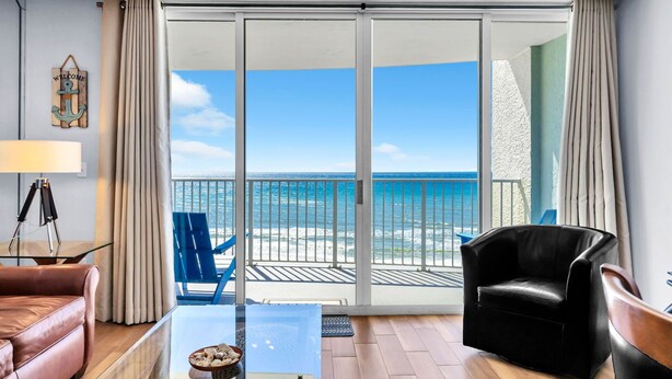 Ein modernes Wohnzimmer mit einem Glastisch, einem Ledersofa, einem schwarzen Sessel und einem Balkon mit Meerblick.