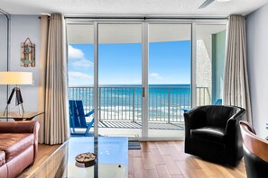 Ein modernes Wohnzimmer mit einem Glastisch, einem Ledersofa, einem schwarzen Sessel und einem Balkon mit Meerblick.