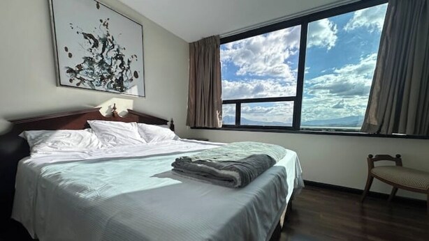 Una habitación de hotel con una cama grande, vistas al cielo a través de una ventana y una silla.