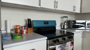 Una cocina con estufa, licuadora y alacenas.