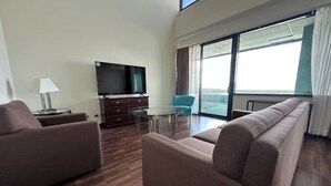 Una sala de estar moderna con un sofá, un televisor, una mesa de vidrio y vistas amplias a través de grandes ventanales.