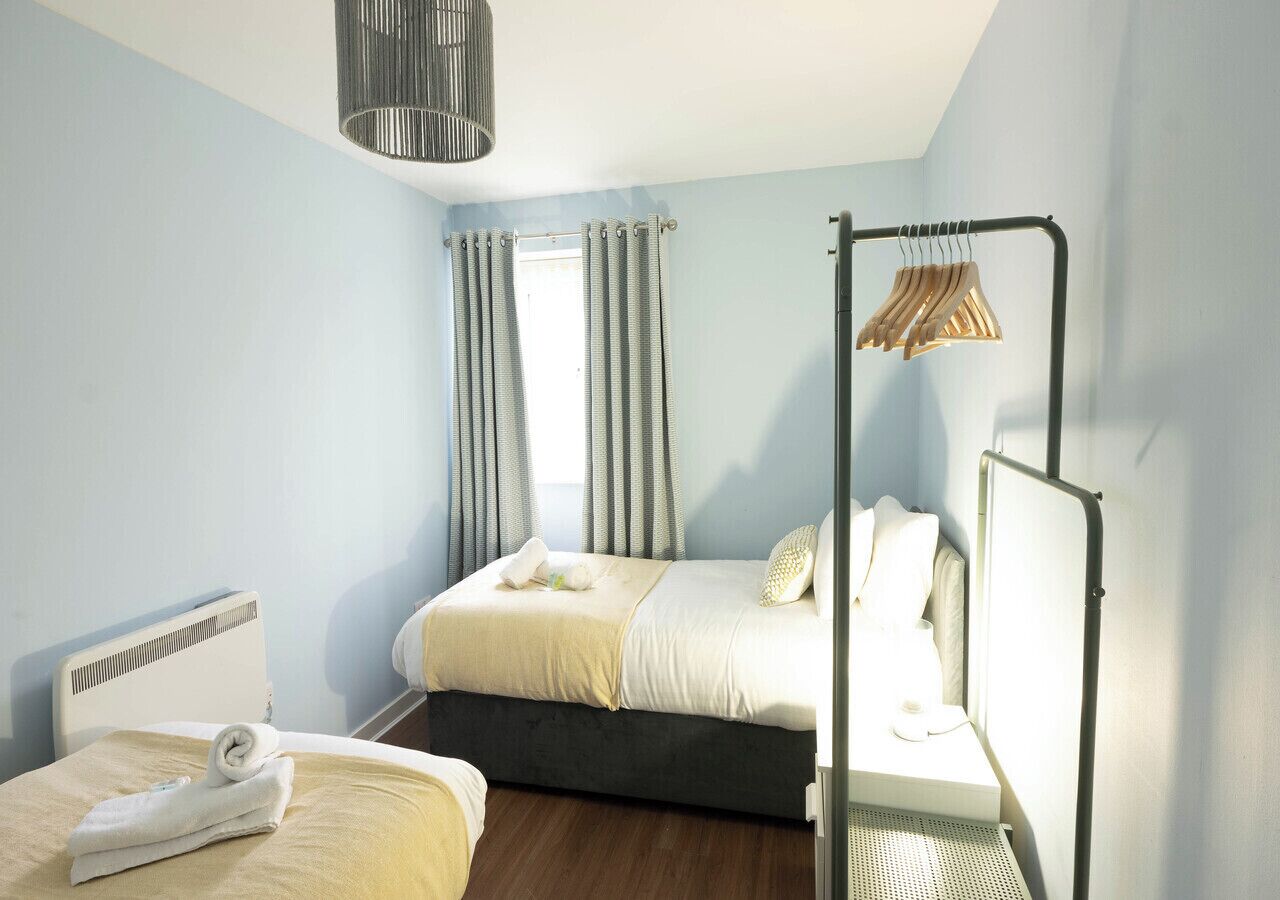 A bedroom with a bed, a bedside table, a hanging light fixture, and a window with curtains.