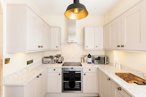A modern kitchen with white cabinets, a stainless steel oven, a microwave, and a wooden cutting board. - Unique Castle Stay, The East Gate Tower, Warwick - Pass the Keys (Warwick)