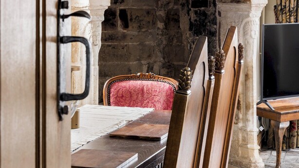 Une pièce avec une cheminée en pierre, un miroir orné d’une sculpture de cheval et une table à manger avec des chaises.