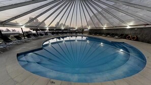 A large indoor swimming pool with a semi-circular shape, surrounded by lounge chairs and a covered area with a roof. - Hotel Marbella Resort (Puchuncavi)