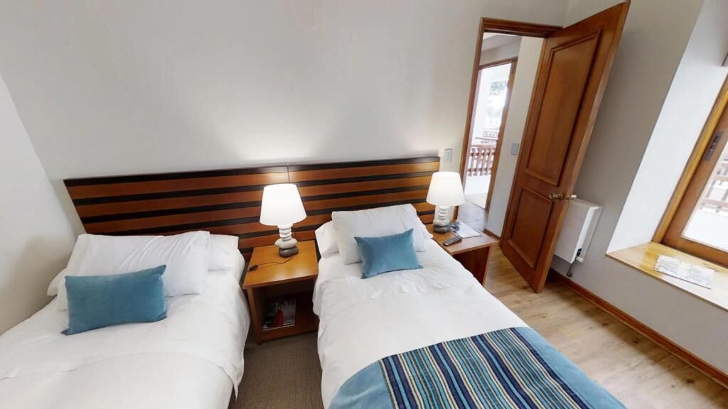 A hotel room with two beds, wooden headboards, bedside tables with lamps, a mirror, and a window.