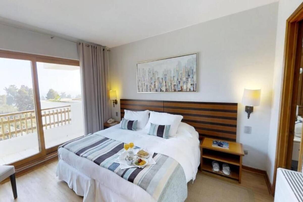 Une chambre d’hôtel avec un grand lit, une chaise, une petite table avec un livre et une vue sur l’extérieur.