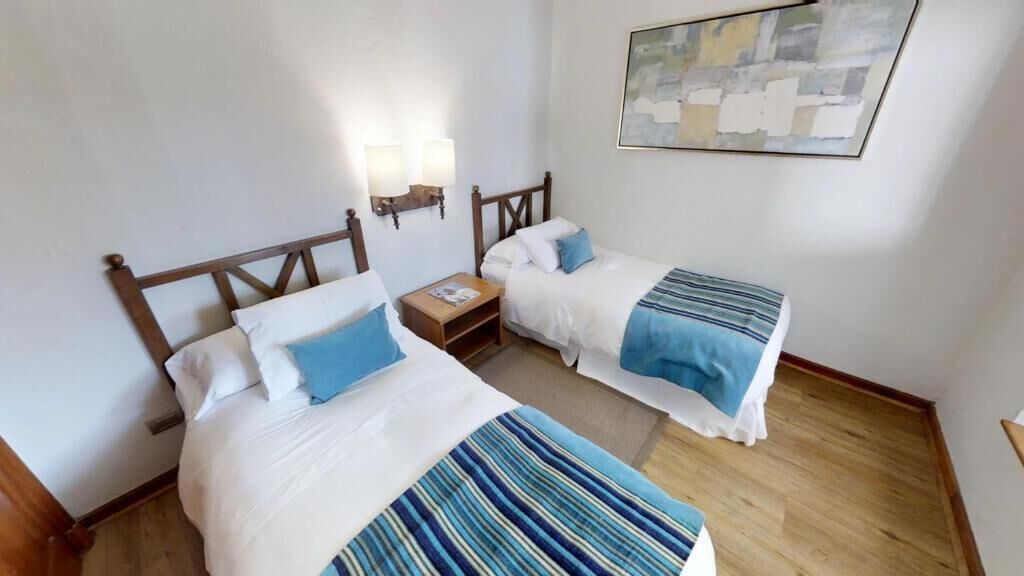 Habitación de hotel con dos camas, una mesita de noche, lámparas de pared y un cuadro en la pared.