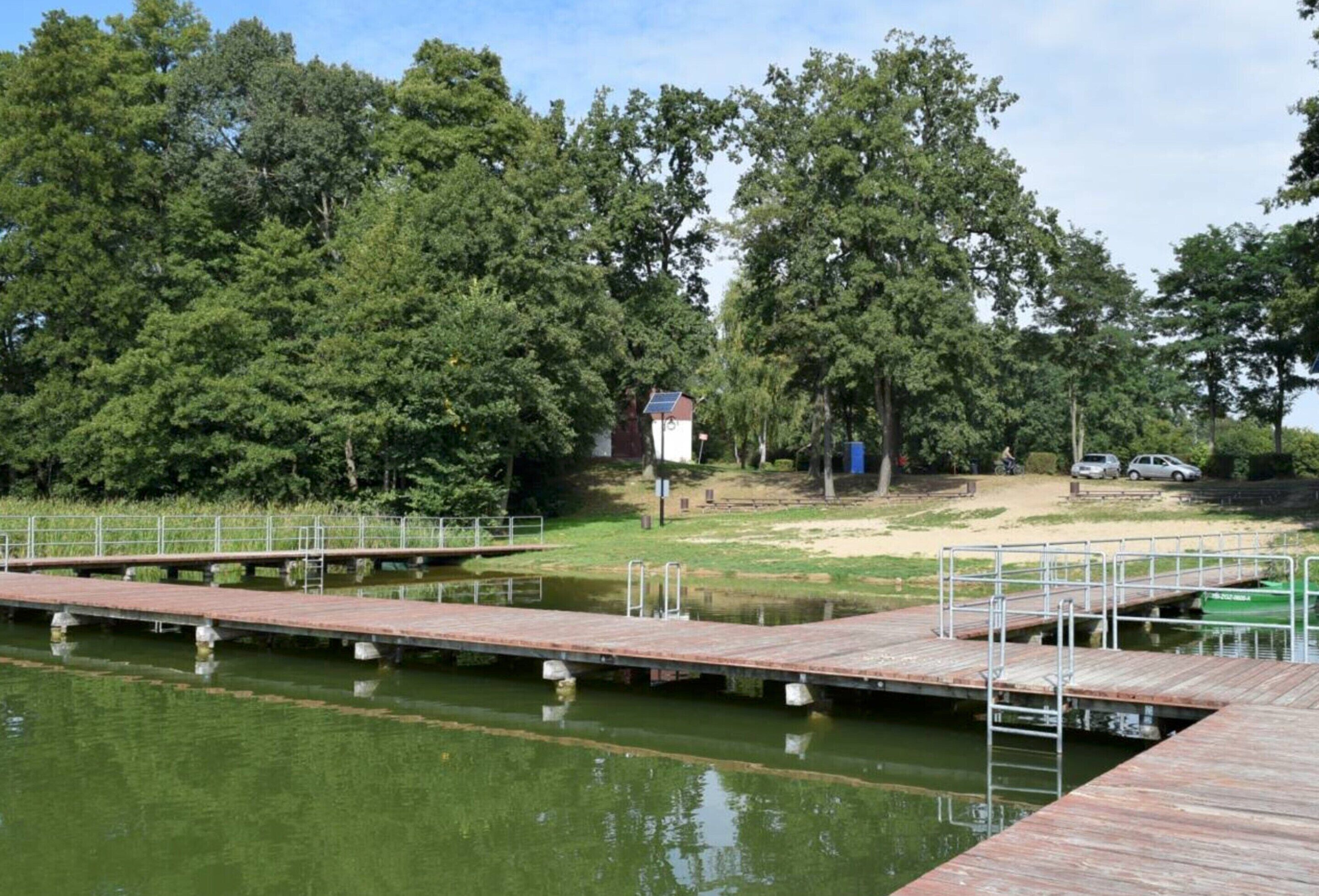 Une jetée en bois s’étendant au-dessus d’une étendue d’eau calme, entourée d’arbres verdoyants et avec un petit bâtiment visible au loin.