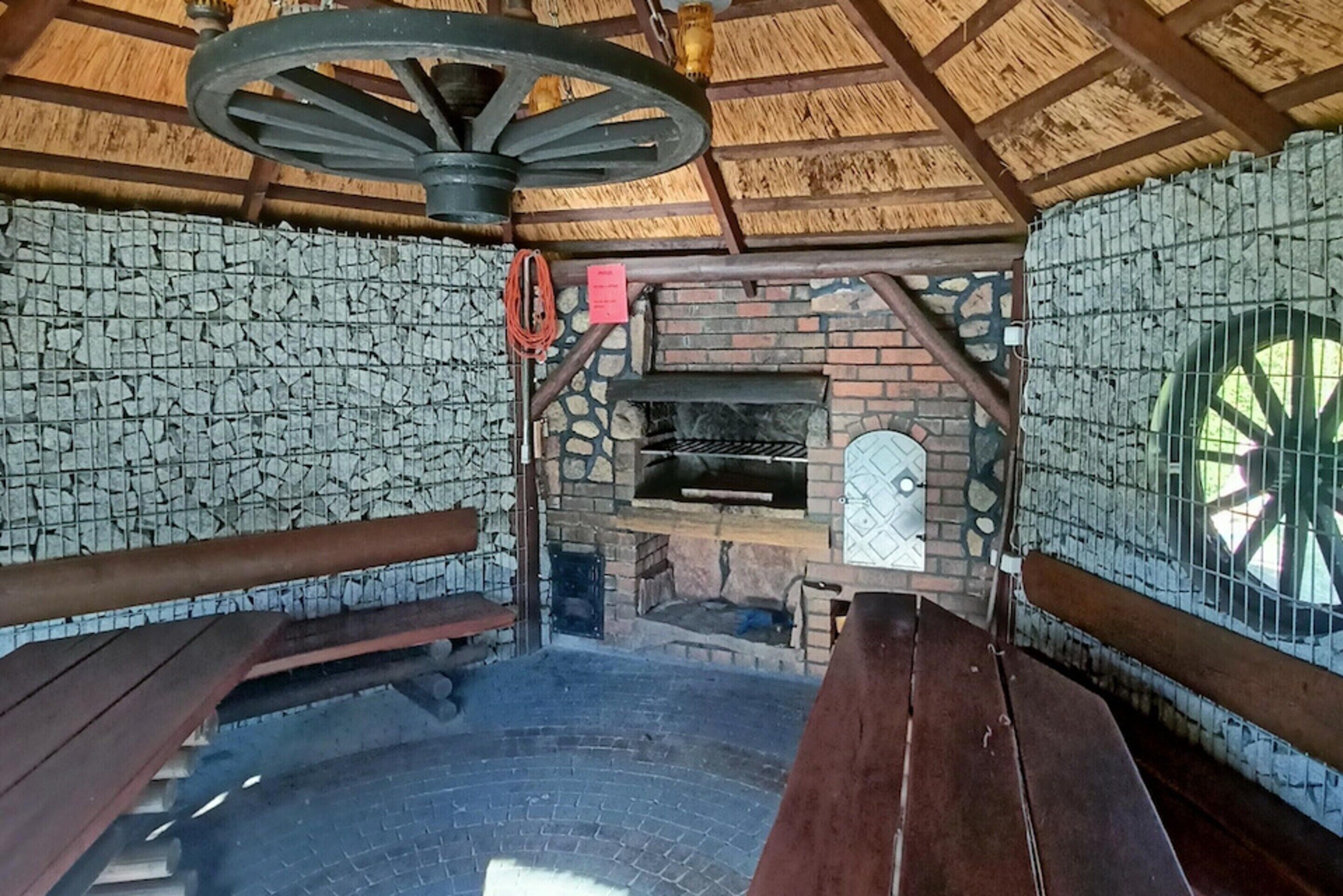 Un espace extérieur rustique aménagé avec des murs en pierre et un sol en briques, comprenant une grande roue et un four en briques.
