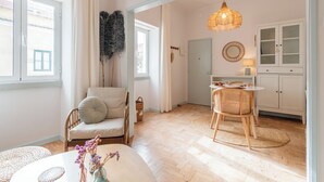 Ein Zimmer mit einer Couch, einem Sessel, einem Tisch, einer Pendelleuchte, einem Schrank und einer Tür.