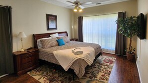 A bedroom with a bed, a nightstand, a lamp, a ceiling fan, a window with curtains, and a potted plant. - Poplar Meadow | King Bed • Gazebo • Pets Welcome! (Canton)