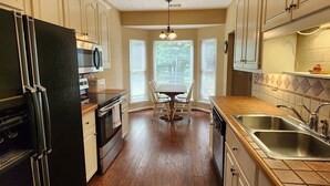 A kitchen with wooden flooring, white cabinets, a black refrigerator, a microwave, a sink, and a dining table with chairs. - Poplar Meadow | King Bed • Gazebo • Pets Welcome! (Canton)