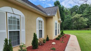 A house with a beige exterior, white shutters, and a landscaped front yard with mulch and small shrubs. - Poplar Meadow | King Bed • Gazebo • Pets Welcome! (Canton)