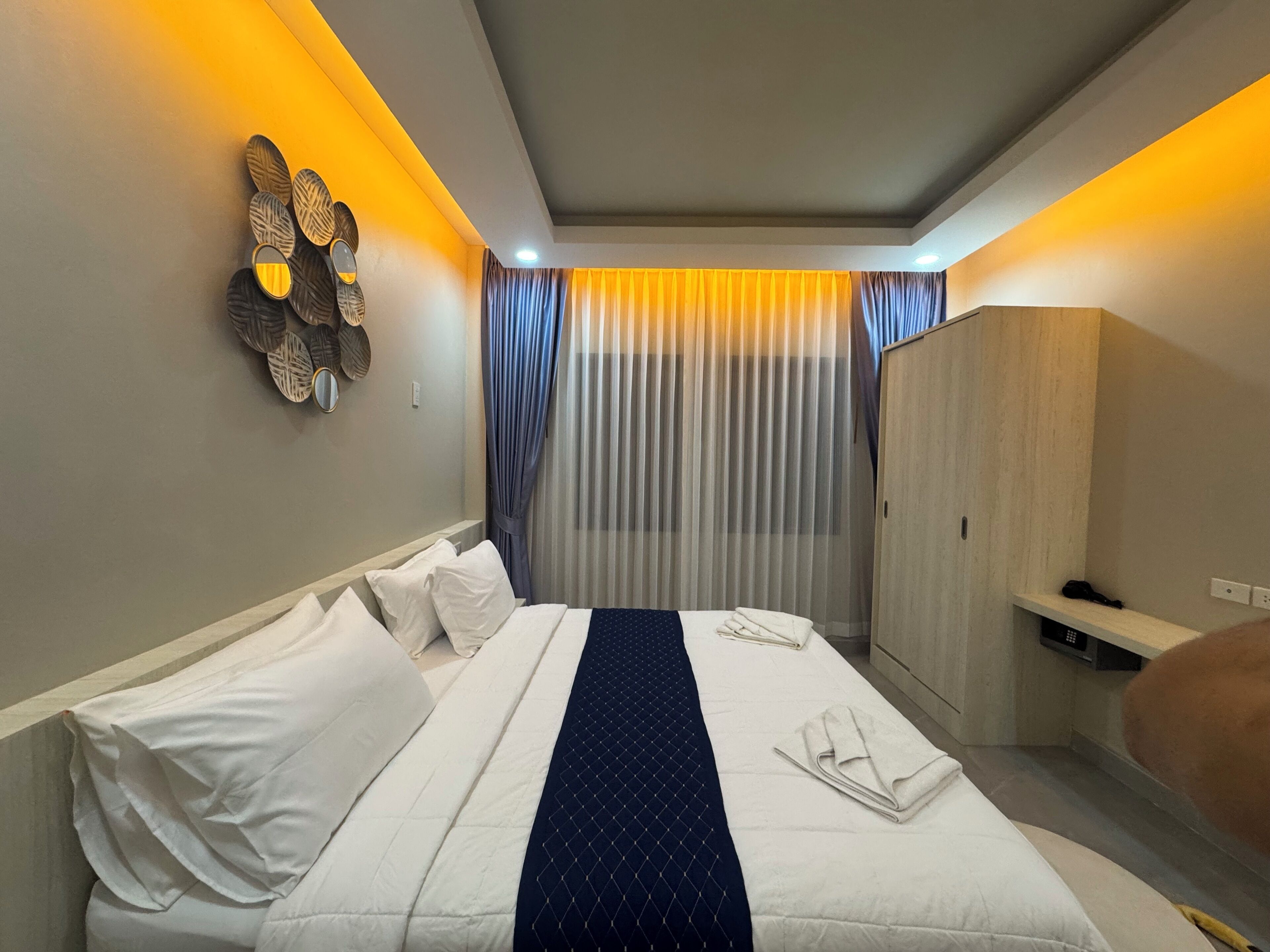 Une chambre d’hôtel équipée d’un lit, d’une armoire, d’un miroir et d’un luminaire fixé au mur.