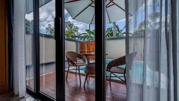 A room with a view of a patio area featuring a pool, chairs, and an umbrella.