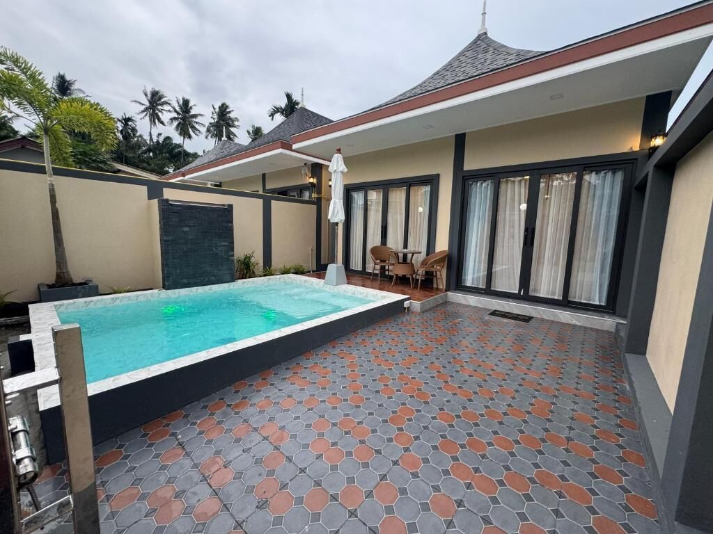 Zwembad met betegeld zonnedek, een overdekte patio en uitzicht op palmbomen.