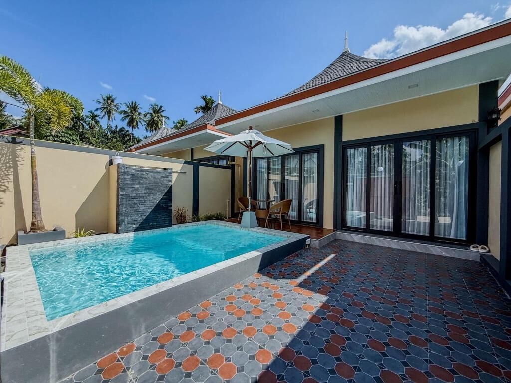 A modern house with a swimming pool, a patio with patterned tiles, and a glass door leading to a covered outdoor area.