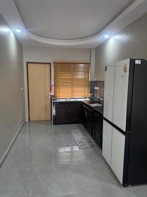 Una cocina moderna con armarios oscuros, un refrigerador negro y piso de baldosas.