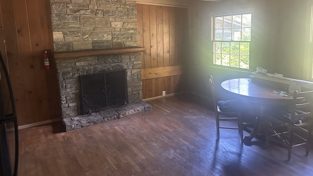 Una habitación con chimenea de piedra, paredes de madera, una mesa de comedor con sillas y una ventana con vistas a zonas verdes.