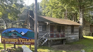Una cabaña rústica de troncos con un porche y un letrero que dice "Pioneer Village Log Cabins by the Stream".