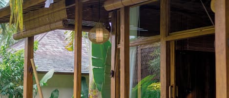 A wooden porch with a bench, surrounded by tropical foliage.