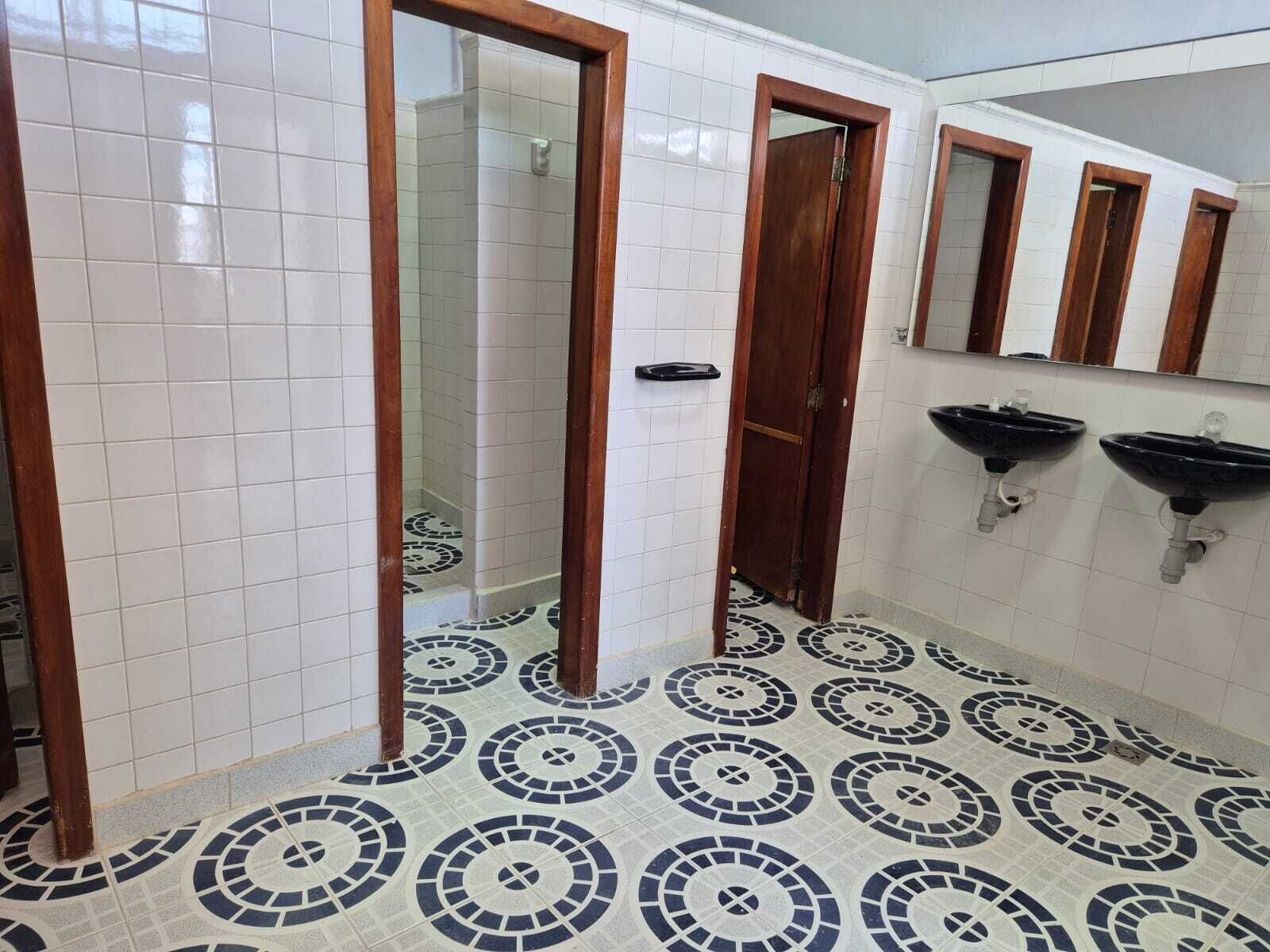 A bathroom with white tiled walls, a patterned floor, and wooden doors. There are two sinks with mirrors above them.