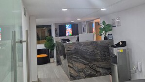 A modern reception area with a marble counter, a water dispenser, and a seating area with a sofa and a chair. - Hostal Capullo de seda (Zapatoca)