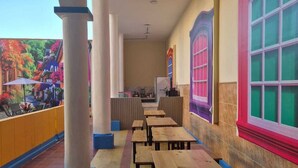 A covered outdoor seating area with wooden tables and benches, a mural on the wall, and a view of colorful buildings. - Hostal Capullo de seda (Zapatoca)