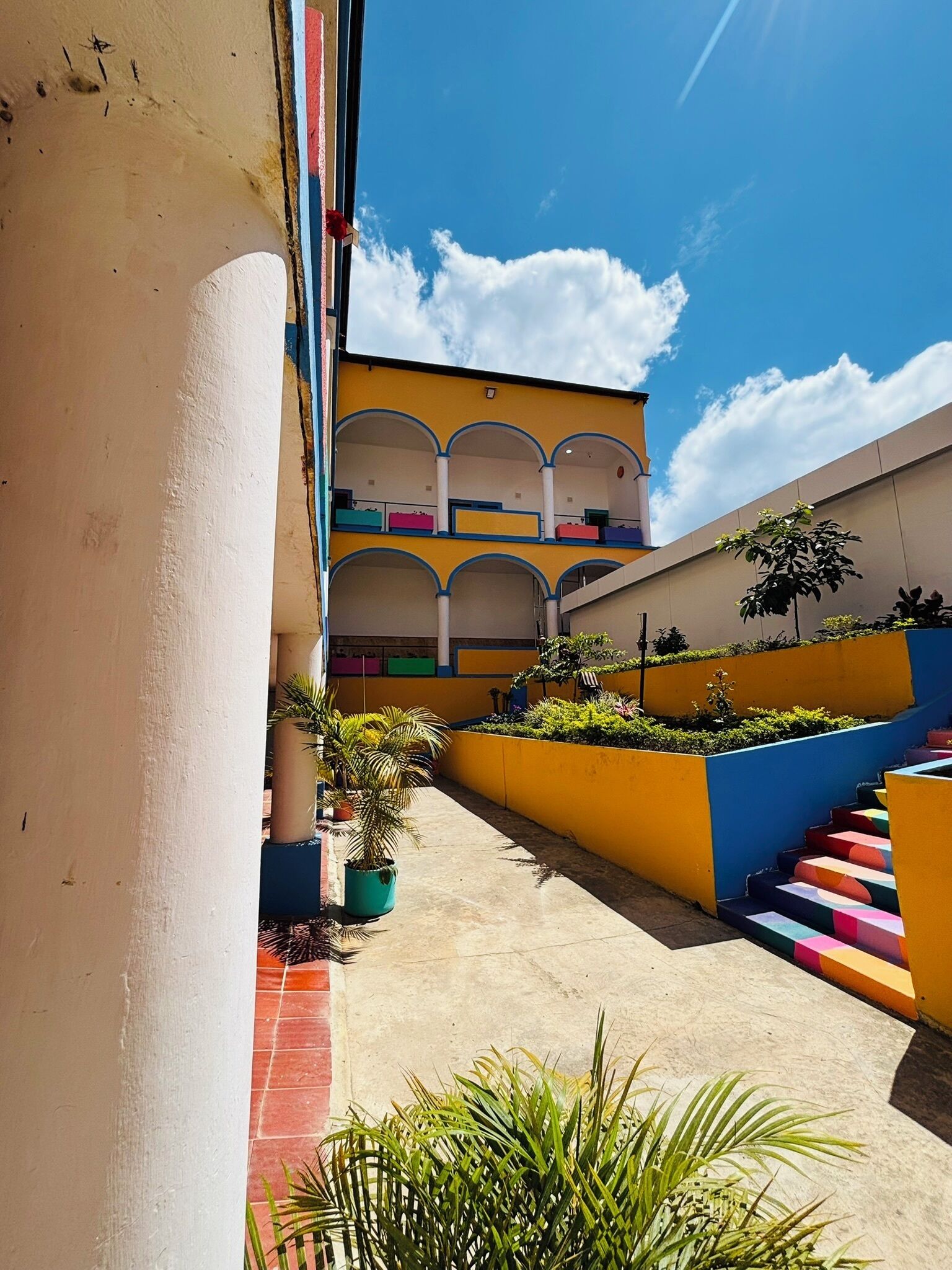 Um edifício com vários níveis, fachada amarela, diversas varandas e escadaria com degraus coloridos.