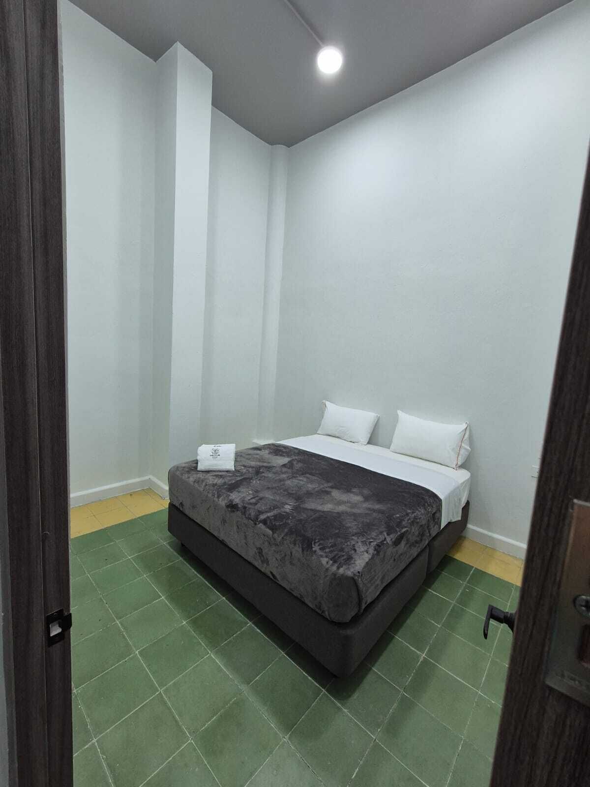 Un dormitorio con cama, paredes blancas y suelo de baldosas verdes.