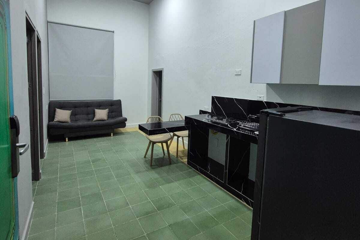 A compact kitchen with a dining area, a sofa, and a refrigerator.