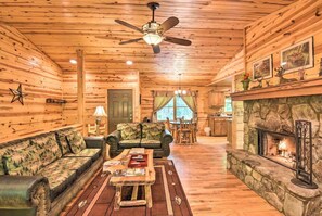 L’intérieur d’une cabane en rondins, avec une cheminée, un ventilateur de plafond, un canapé, une table basse et un coin repas.