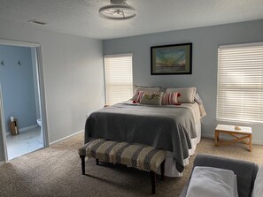 A bedroom with a bed, two windows with blinds, a ceiling fan, a painting on the wall, and a small bedside table. - 3-bedroom house in pleasant Palm Coast with cool AC (Palm Coast)