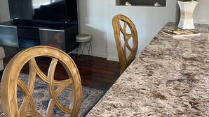 A modern kitchen with a granite countertop, wooden chairs, a dining table, a television, and decorative shelves. - 3-bedroom house in pleasant Palm Coast with cool AC (Palm Coast)