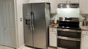 A kitchen with a stainless steel refrigerator, a stove, and white cabinets. - 3-bedroom house in pleasant Palm Coast with cool AC (Palm Coast)