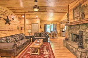 A log cabin interior with a fireplace, wooden walls, a sofa, a coffee table, and a dining area. - Highline 4 bdrm Cabin! Pool Table! Near Helen! (Clarkesville)