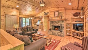 Ein rustikaler Innenraum einer Blockhütte mit Kamin aus Stein, Holzmöbeln und einem Fernseher auf einem Regal.