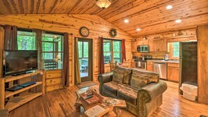 A cabin interior with a wooden interior, a television, a couch, a dining table, and a kitchen area.