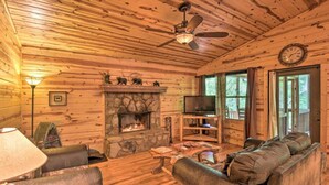 A cozy log cabin interior with a stone fireplace, a television, and a comfortable seating area.