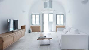 Uma sala de estar moderna com uma TV em um móvel de madeira, um sofá branco e uma mesa de centro.